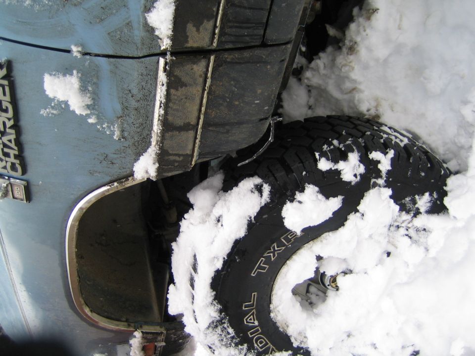 Side panel and tire of a light blue vehicle stuck in snow. Text on the vehicle reads 'CHARGER'