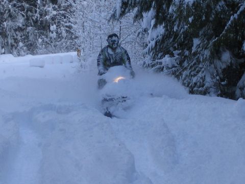 1990 Ford Bronco - Rider on a snowmobile navigates through deep snow in a wooded area.