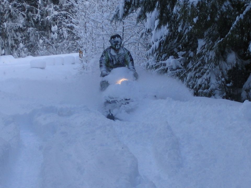 Snowmobile kicking up snow, rider wearing goggles and camouflage jacket