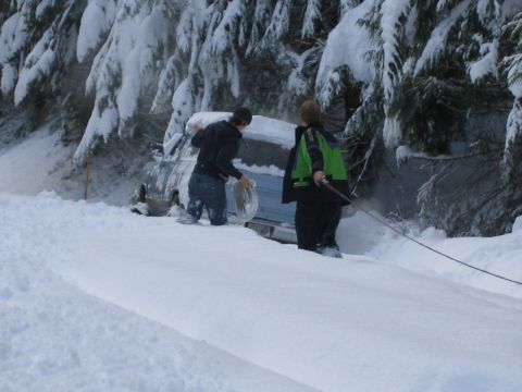 1990 Ford Bronco - Two individuals are attempting to free a vehicle that is stuck in a snow-covered area, possibly a roadside or trail.