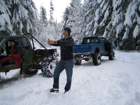 1990 Ford Bronco - Two lifted off-road vehicles are parked in a snowy forest scene.
