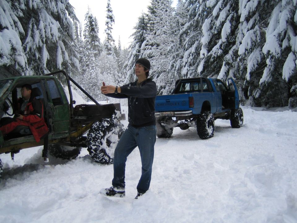 Two modified off-road vehicles parked in a snow-covered forest with a man standing between them
