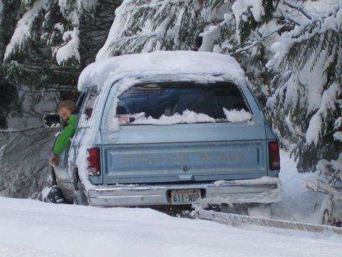 1990 Ford Bronco - A light blue SUV is partially buried in snow, with a child visible in the driver's side window.