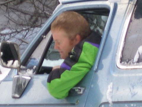 1990 Ford Bronco - A man in a bright green jacket leans out the window of a 1990 Ford Bronco, with snow visible on the vehicle and trees in the background.