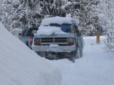 1990 Ford Bronco - A blue pickup truck navigates a snow-covered road, with another vehicle visible behind it.