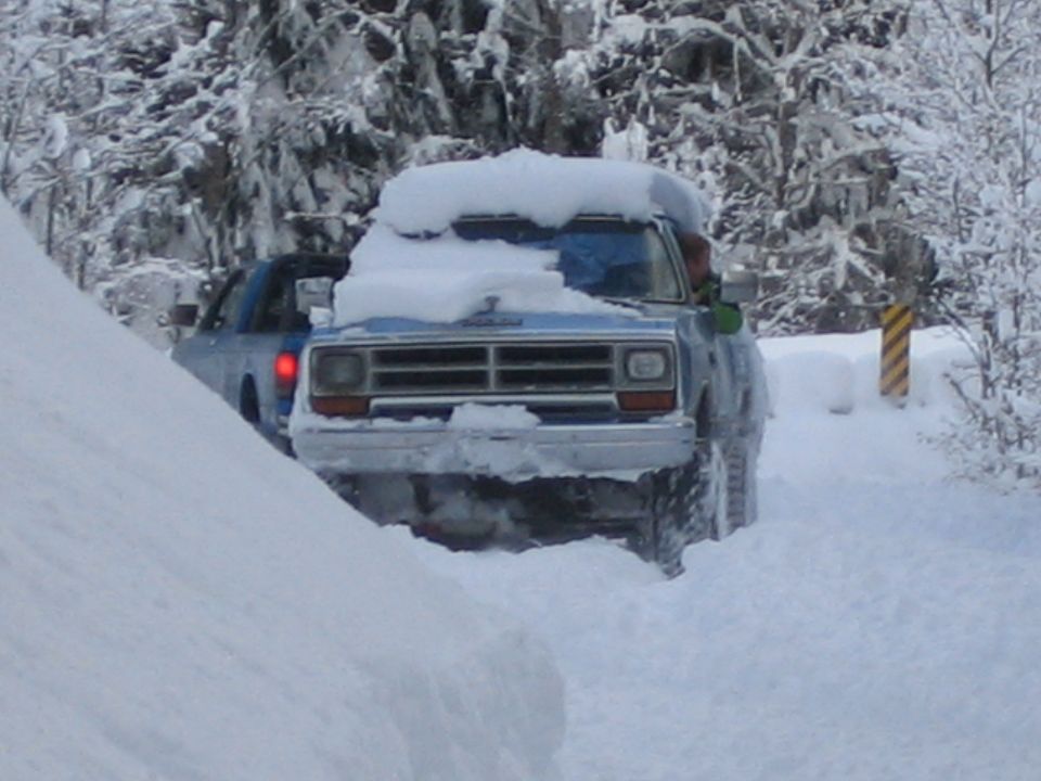Blue pickup truck driving in deep snow, another vehicle behind it