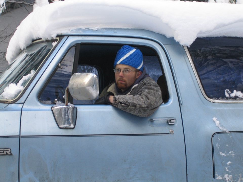 Light blue 1980s SUV side view with man wearing blue hat inside
