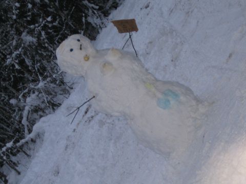 1990 Ford Bronco - A snowman is depicted lying down in a snowy environment, adorned with simple features and a small sign.