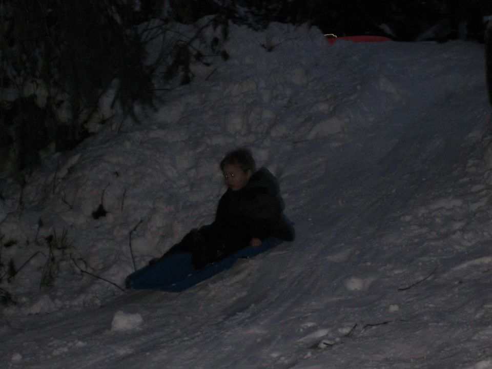 Child on a blue sled going down a snow-covered slope at night