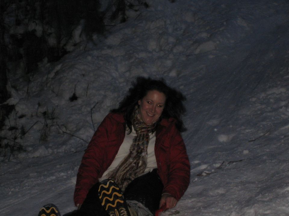 Woman in red jacket and scarf sledding down a snowy hill at night