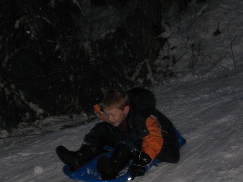 1990 Ford Bronco - A boy rides a sled down a snowy hill at night.