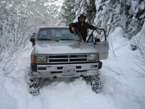 1990 Ford Bronco - Toyota pickup truck with off-road tires navigates deep snow in a wooded area.