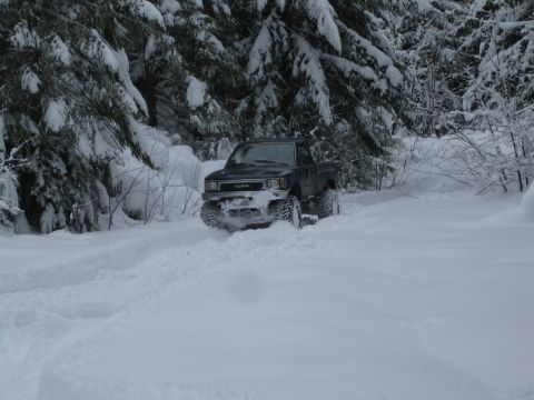 1990 Ford Bronco - A Toyota pickup truck navigates a snow-covered forest road, kicking up powder as it goes.