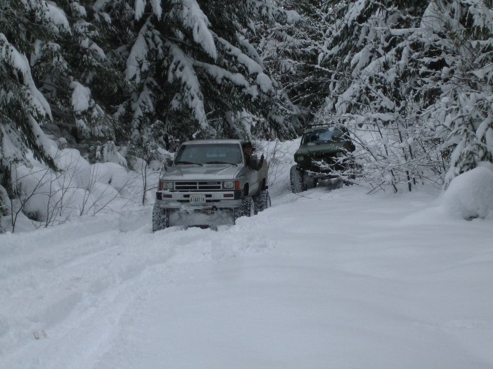 Silver Toyota pickup truck and green SUV driving on a snowy forest road