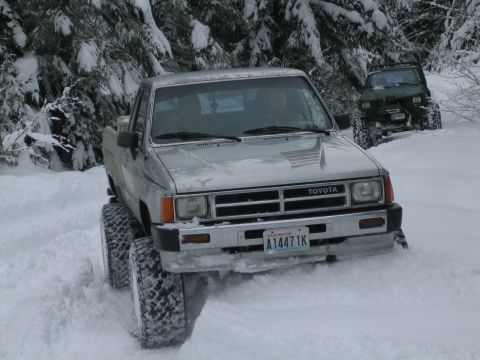 1990 Ford Bronco - A silver Toyota pickup truck navigates a snowy terrain, with another off-road vehicle visible in the background.
