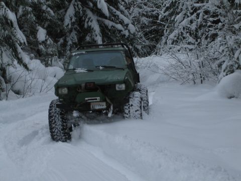 1990 Ford Bronco - A green 1990 Ford Bronco navigates a snowy forest road, its large tires kicking up powder.