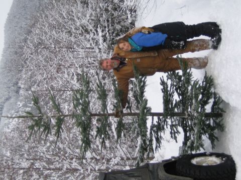 1990 Ford Bronco - A couple poses with a freshly cut Christmas tree in a snow-covered forest. A portion of a vehicle is visible in the lower right corner.