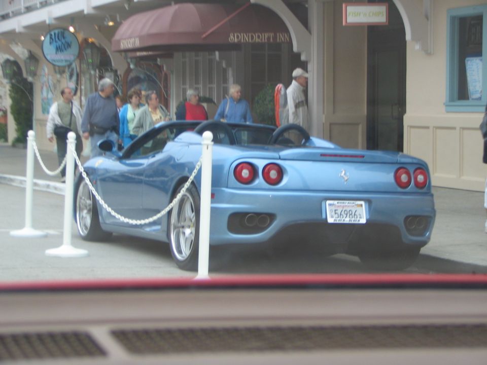 blue convertible sports car parked outside a building with people walking by