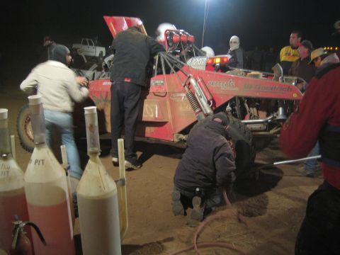 1990 Ford Bronco - pit crew services a red number-1207 off-road buggy at night, fuel jugs lined up in the foreground.