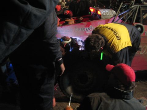 1990 Ford Bronco - crew member in a yellow BFGoodrich shirt leans over a tire while servicing a red off-road buggy at night.