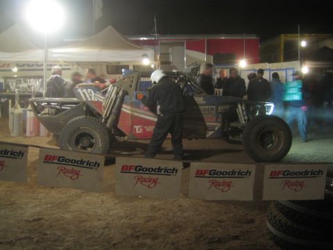 1990 Ford Bronco - off-road race buggy sits in a lit pit area fronted by a row of BFGoodrich Racing banners at night.