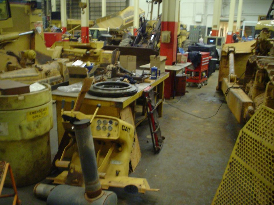 Interior of a heavy machinery repair shop with multiple yellow bulldozers and equipment