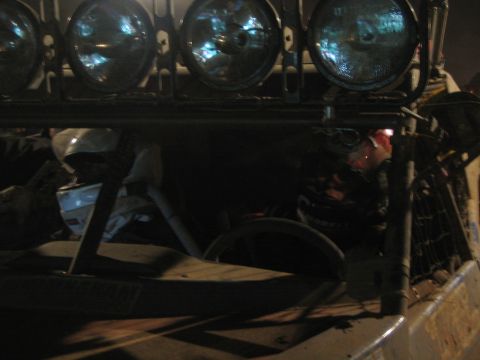 1990 Ford Bronco - dim night close-up of a helmeted driver seated beneath a roof light bar of skull-graphic lamps.