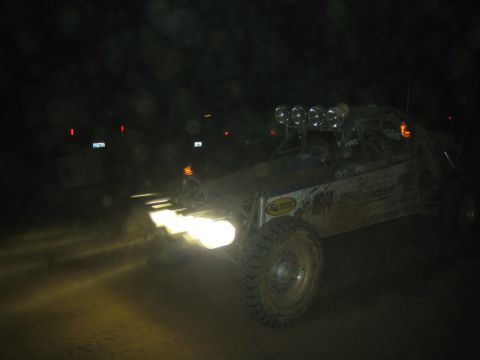 1990 Ford Bronco - single-seat off-road race buggy with a row of roof lights kicks up dust during a nighttime desert race.