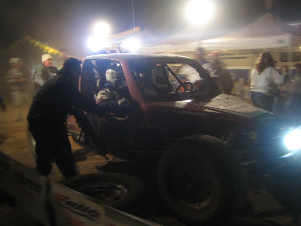 Crew member working on a red off-road race truck under tent lights at night