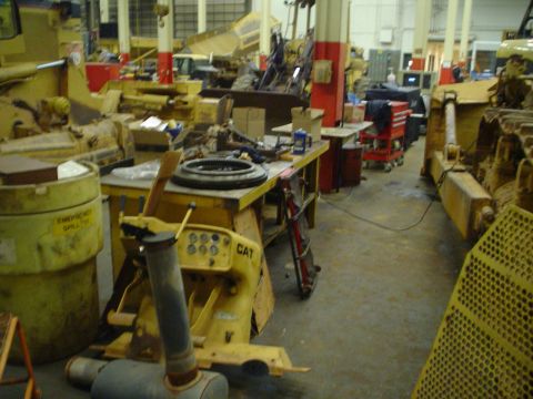 1966 International School Bus - A workshop scene filled with yellow construction equipment, including bulldozers and parts laid out on workbenches.