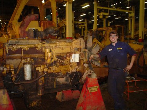 1966 International School Bus - A worker poses with a large diesel engine, likely undergoing maintenance or assembly in a heavy machinery facility.