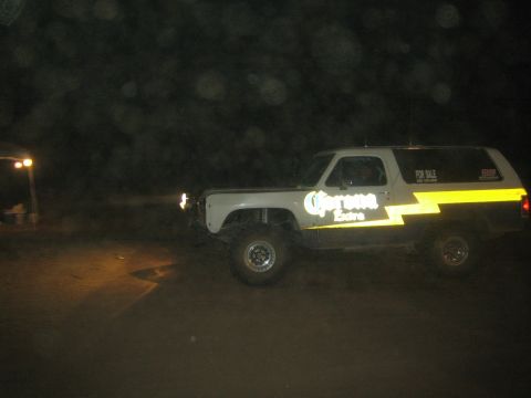 1990 Ford Bronco - lifted two-door SUV in two-tone paint with Corona Extra graphics and a For Sale sign sits on dirt at night.