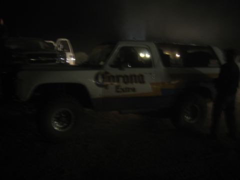 1990 Ford Bronco - lifted two-door SUV in Corona Extra livery is shown in profile at night as a person stands at the right.