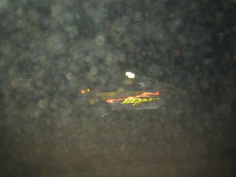 1990 Ford Bronco - yellow off-road race buggy with flame graphics is partly obscured by a heavily dust-spotted lens at night.