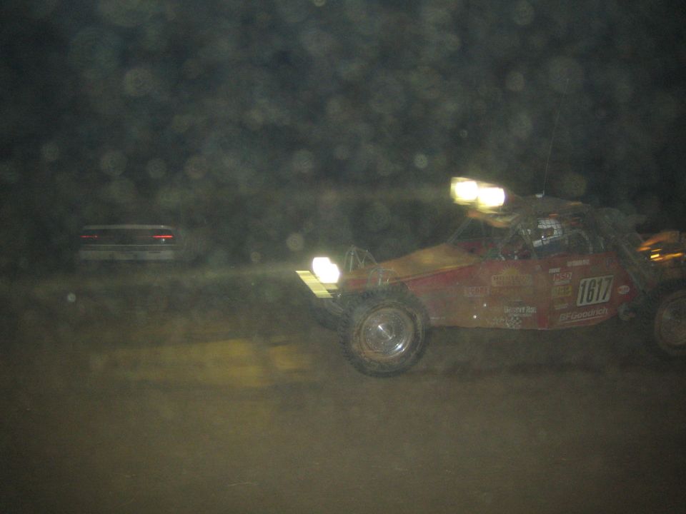 Red off-road race buggy number 1617 racing at night through dust