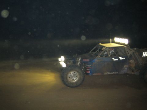 1990 Ford Bronco - blue off-road race buggy numbered 122 with a roof light bar and BFGoodrich tires races across dirt at night.