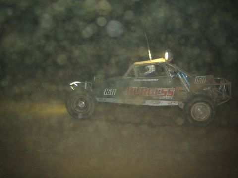 1990 Ford Bronco - off-road race buggy lettered Burgess Motorsports and numbered 1611 races at night, seen through a dusty lens.