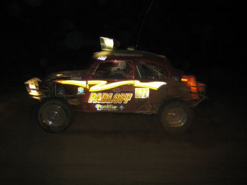 1990 Ford Bronco - Volkswagen Beetle-bodied off-road racer lettered PABLOFF and numbered 517 speeds past at night with motion blur.