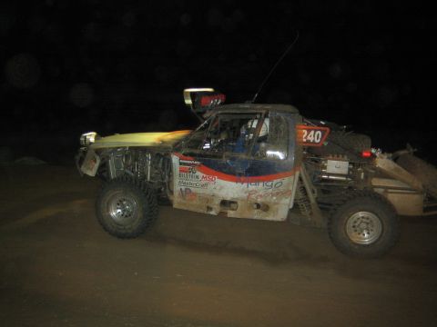 1990 Ford Bronco - mud-splattered off-road race truck numbered 240 with Bilstein and MSD decals runs across dirt at night.