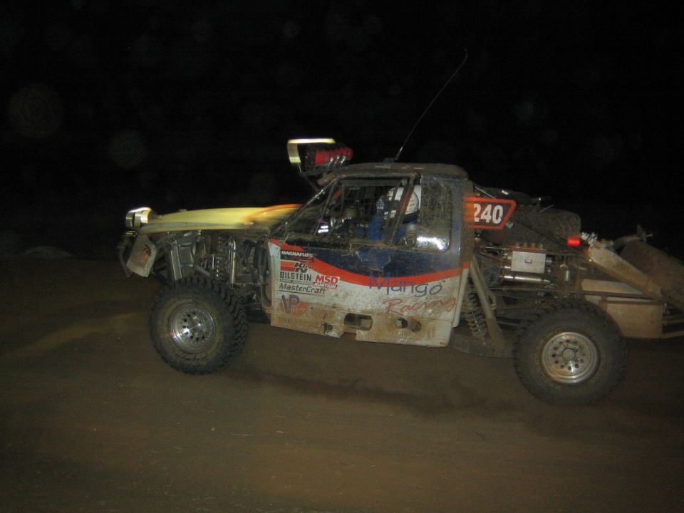 Muddy off-road race truck number 240 with sponsor decals at night
