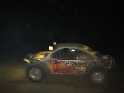 1990 Ford Bronco - Volkswagen Beetle-bodied off-road racer numbered 517 with red graphics speeds across the dirt at night.