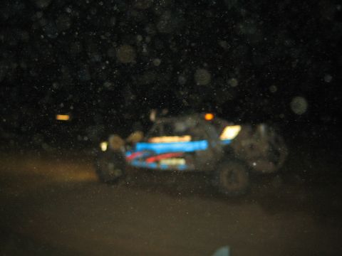 1990 Ford Bronco - blue and red off-road race buggy sits in the dark, barely visible through a speckled, dusty lens at night.