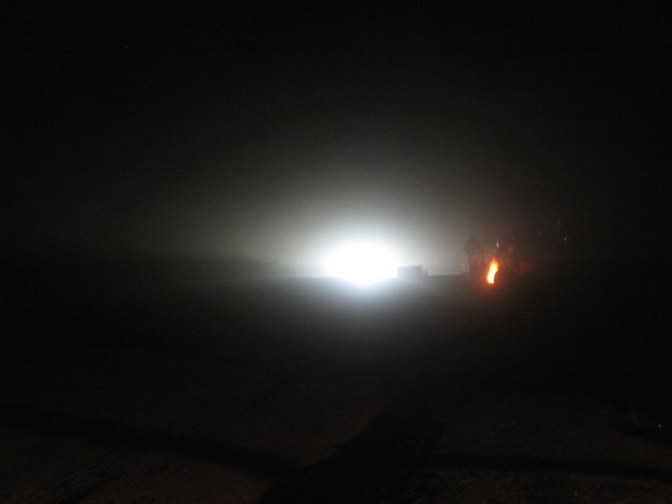Bright headlight glare in darkness with small orange flame to the right