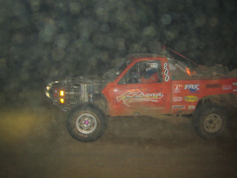 Red off-road race truck number 800 racing through dust at night