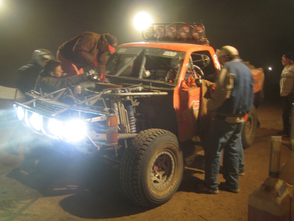 Crew servicing orange race truck 800 with headlights on at night