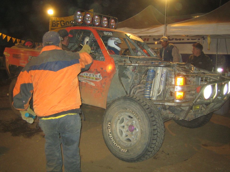 Man in orange jacket beside muddy orange race truck 800 at night