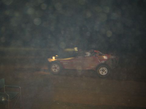 1990 Ford Bronco - dark red off-road race buggy numbered 700 drives through a hazy, dust-filled scene at night.