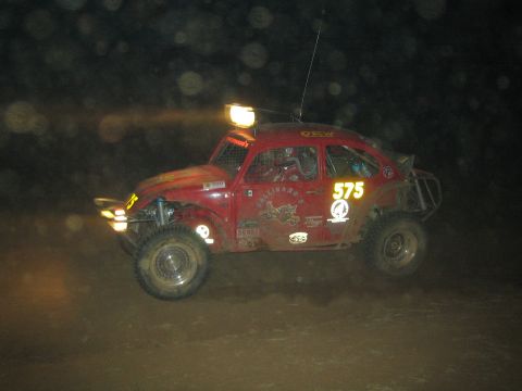 1990 Ford Bronco - red VW-based Baja Bug numbered 575 with a roof-mounted light races over rough terrain at night.
