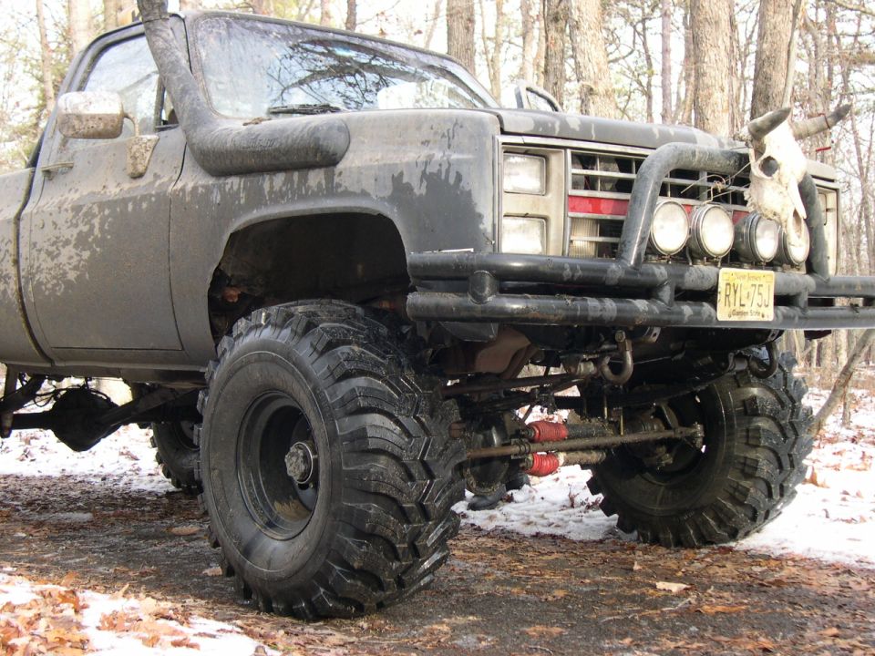 Lifted muddy square-body Chevrolet pickup on large tires with bull skull on the bumper