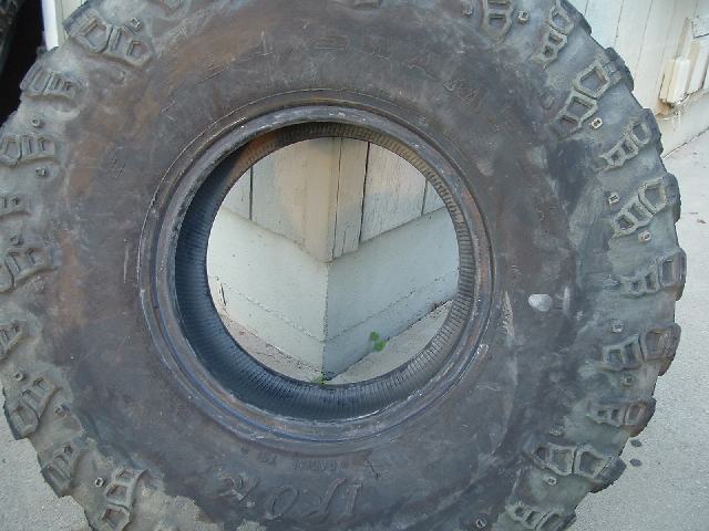 Upright off-road mud-terrain tire leaning against a wooden fence outdoors